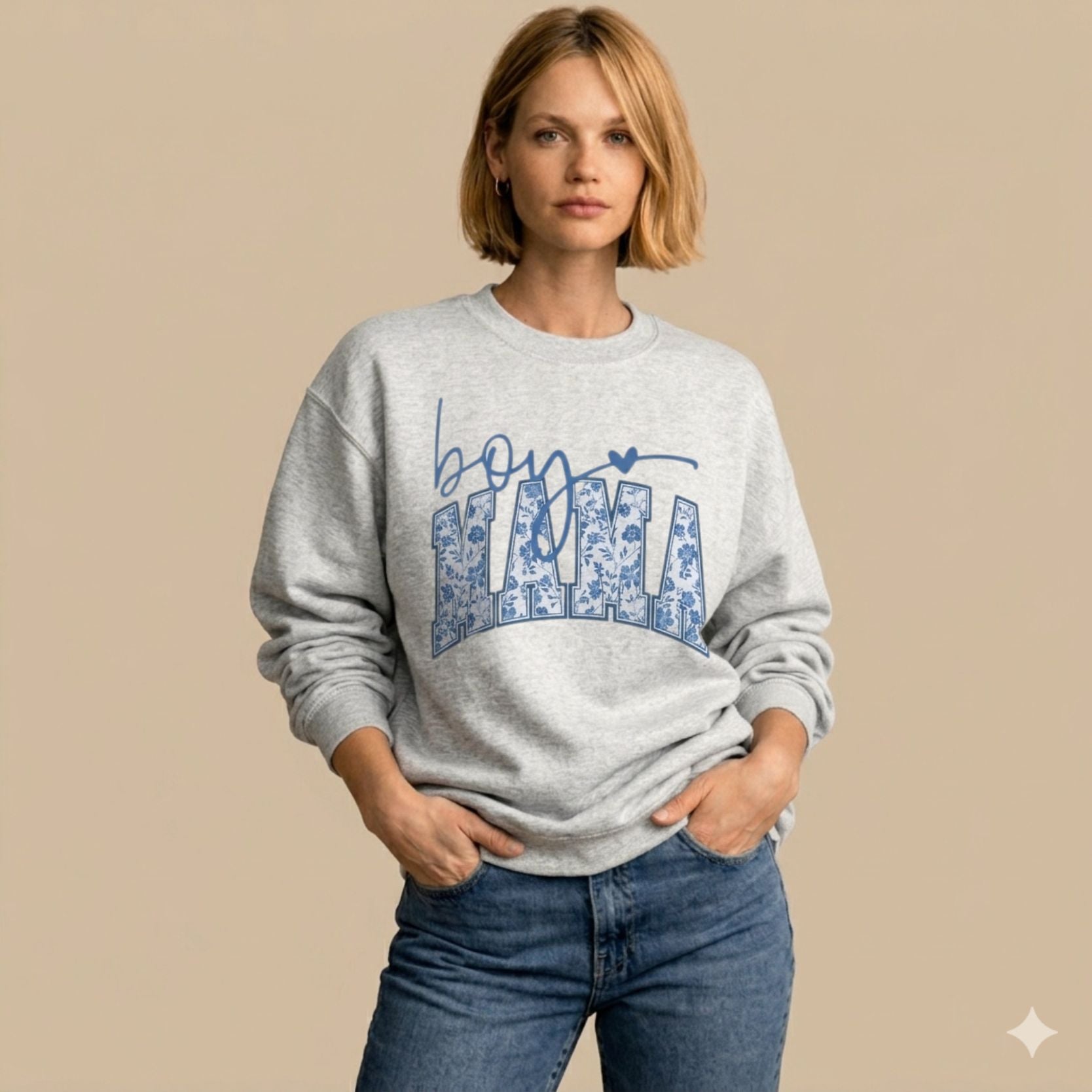 Woman wearing an Ash Boy Mama floral toile varsity crewneck sweatshirt standing against warm beige background with hands relaxed  in her pockets