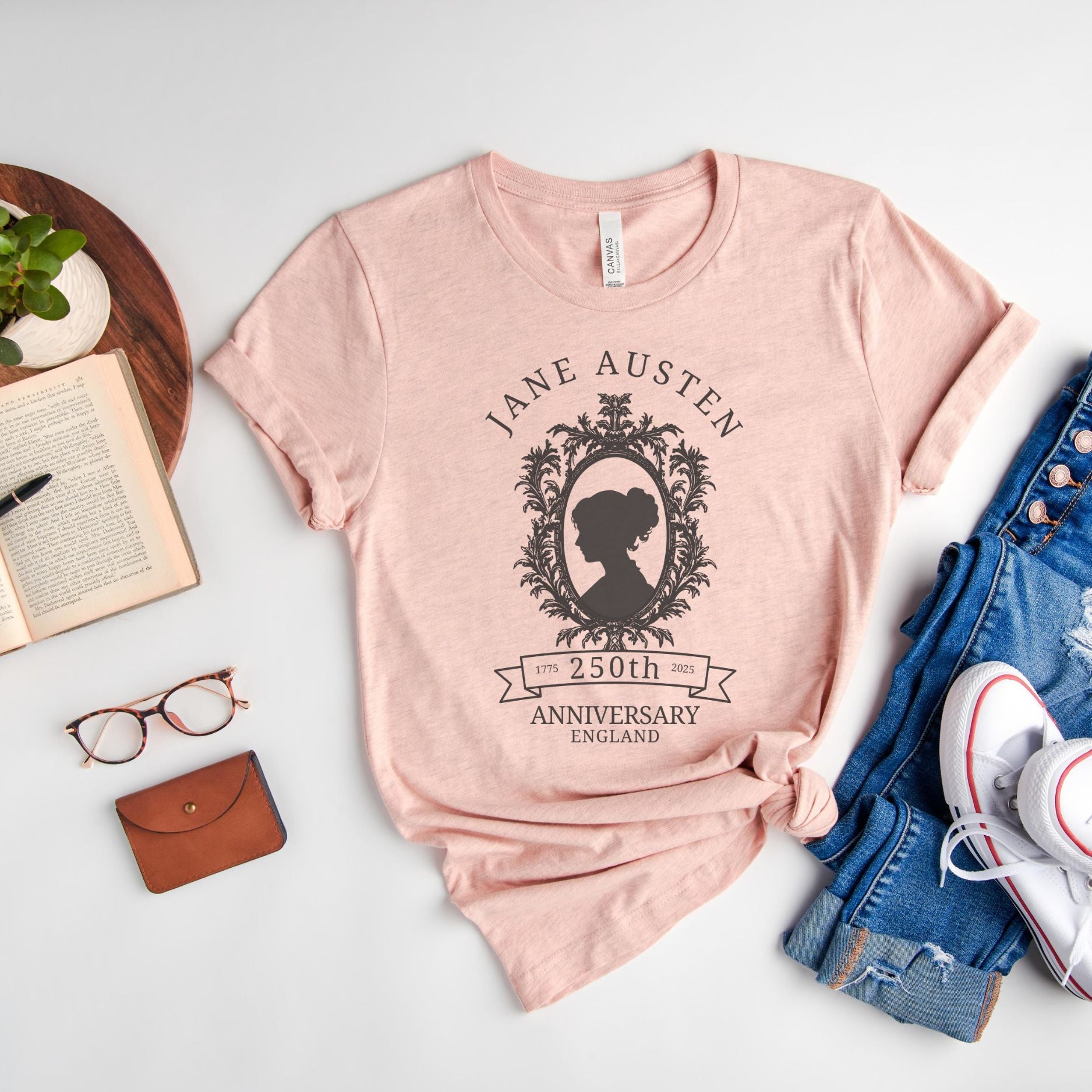 Jane Austen 250th Anniversary heather prism peach, a pink salmon color t-shirt with cameo silhouette surrounded by a book and reading glasses