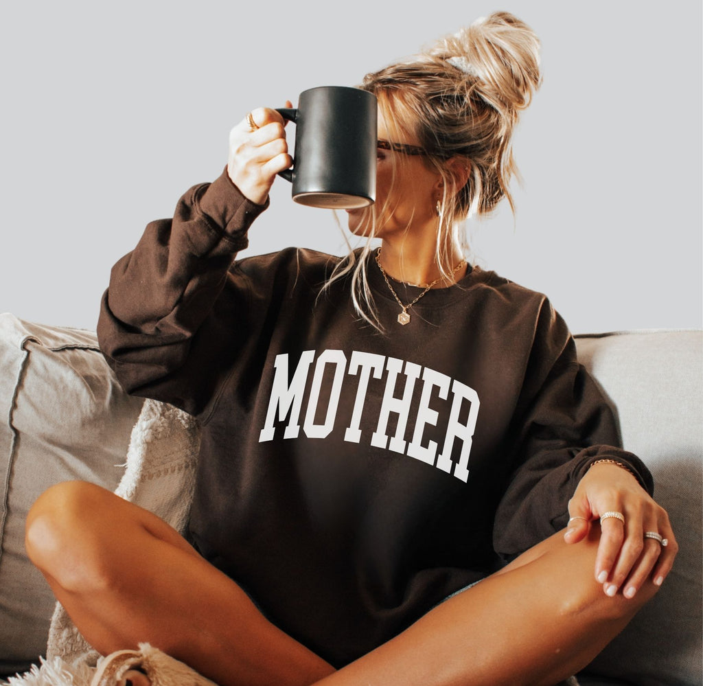 Woman wearing preppy brown Mother sweatshirt with collegiate text in white